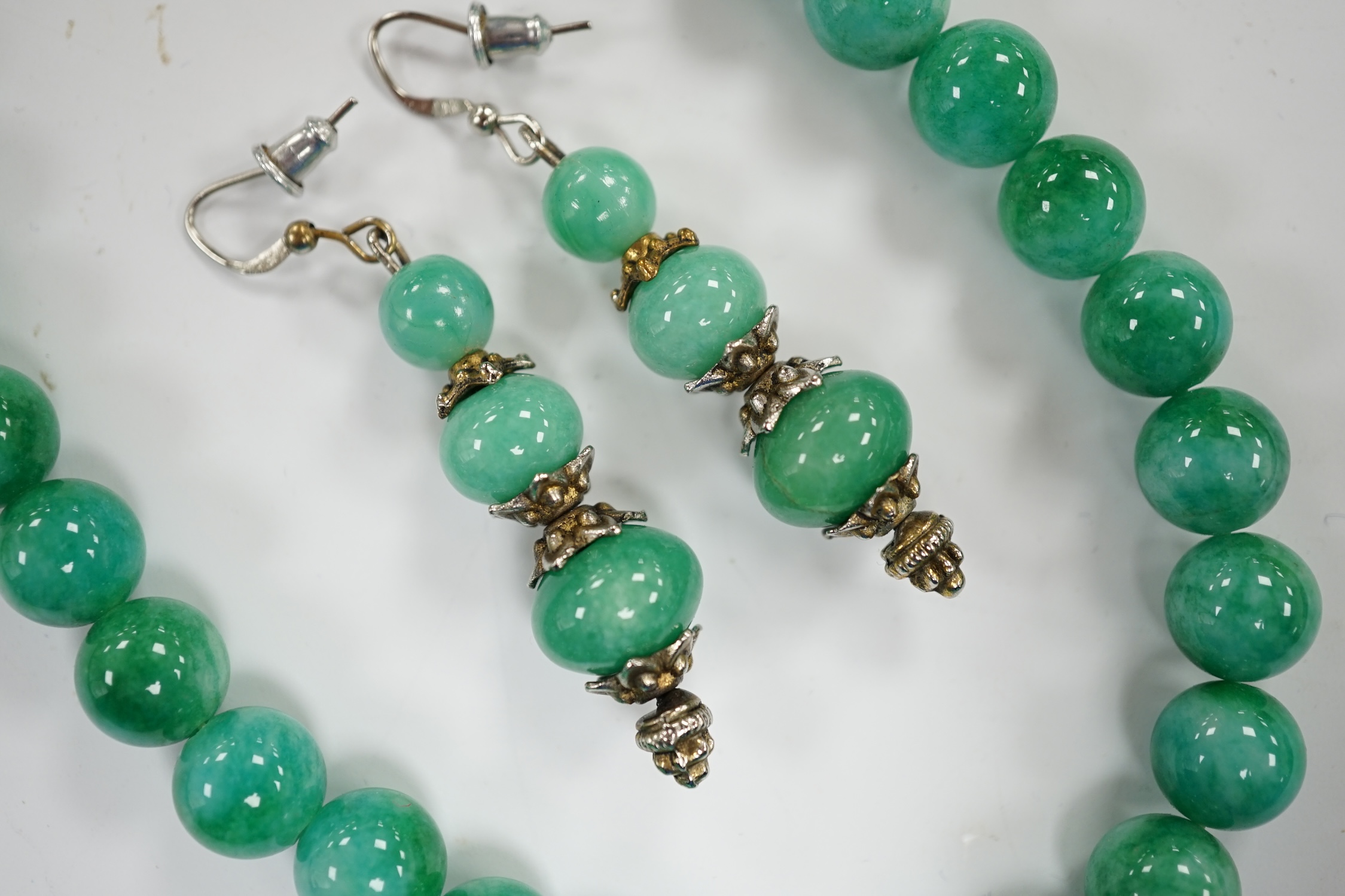 A single strand jadeite bead necklace, 41cm and a pair of jadeite earrings, stamped 18k.